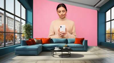 Beautiful young woman wearing casual clothes standing isolated over background surfing on the internet via phone looking at mobile screen Wall mural