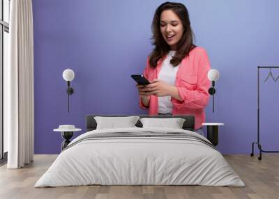 brunette young woman with shoulder-length hair in a pink shirt sits in the internet online from the phone and isolated on a solid background Wall mural