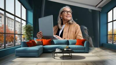 Business senior woman working on a laptop online against the backdrop of an office building Wall mural