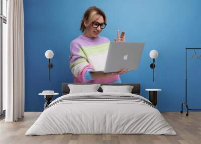 business woman in a striped jacket works with a laptop in her hands on a blue background with copy space Wall mural