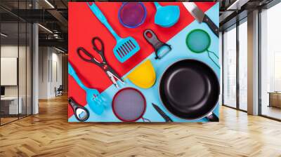 Close up portrait of frying pan with set of kitchen utensils on red-blue background Wall mural