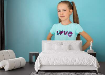 Fashionable teenager girl in blue t-shirt gesticulates, portrait isolated on blue background Wall mural