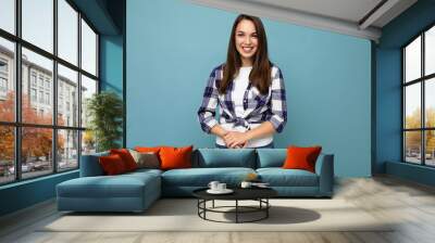 Photo portrait of young beautiful smiling hipster brunette woman in trendy blue and white shirt and jeans clothes. Sexy carefree female person posing isolated near blue wall with empty space in studio Wall mural