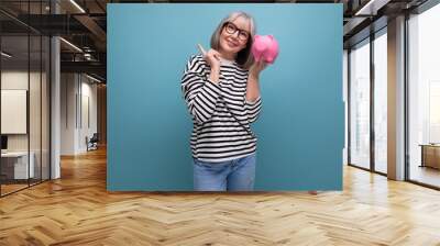 pleasant middle-aged woman 50 years old holding a piggy bank with savings on a bright background with copy space Wall mural