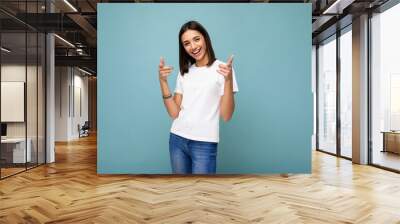 Portrait of young beautiful happy smiling brunette woman wearing trendy white t-shirt with empty space for mock up. Sexy carefree female person posing isolated near blue wall in studio with free space Wall mural