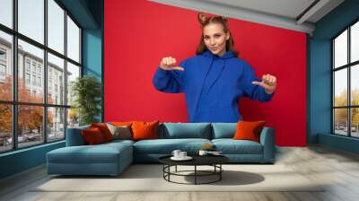 Portrait photo of young fascinating beautiful attractive positive happy cool blonde woman with two horns with sincere emotions wearing trendy hipster blue hoodie isolated over red background with Wall mural