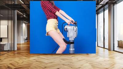 Pretty slim sexy builder girl in red chechered shirt, build goggles and build helmet hold jackhammer Wall mural