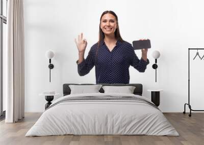 young charming positive successful woman with black hair dressed in a blue blouse holding a smartphone Wall mural