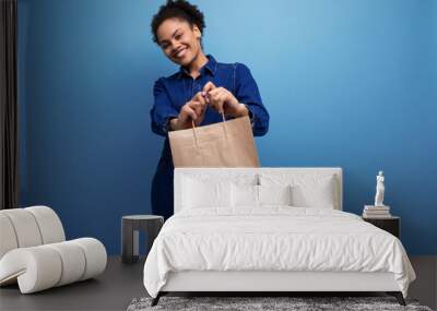 young successful woman with dark skin and black curly hair dressed in a blue denim suit holding a craft brown bag Wall mural