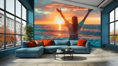 Young woman with her hands up against the background of the sea and sunset on the beach, backwards
 Wall mural