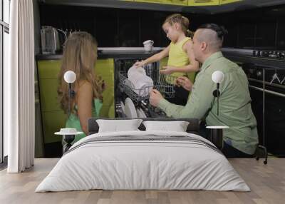 Mother and father teaching daughter learning to use dishwasher. Stylish modern Built In Kitchen Appliances in green black. Mistress girl children loading putting dirty dishes in automatic dishwasher. Wall mural