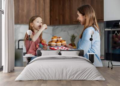 Attractive mother and her little cute daughter are making muffins together in kitchen Wall mural