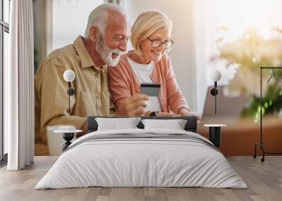 Senior couple sit at a table in the living room with laptop,working from home office Wall mural