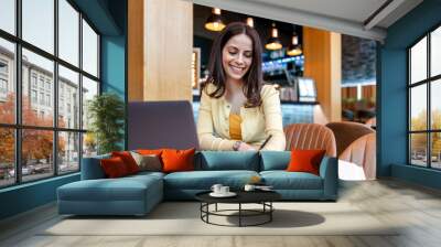 Young businesswoman using laptop while working in a modern coffee shop Wall mural