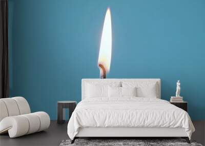 Close-up of a single wax candle burning. Isolated glowing candle on a blue background. Background or illustration of a festive ceremony, a celebration, birthday or Christmas. Wall mural