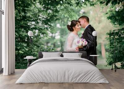 Bride closes her eyes leaning to groom's neck under green tree b Wall mural