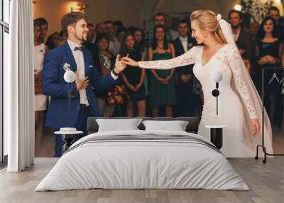 Handsome groom in blue suit takes bride's hand while he dances w Wall mural