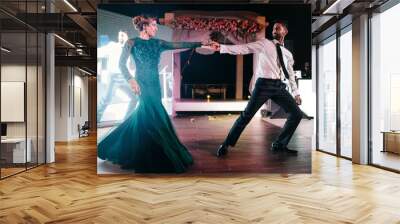 Indian groom in a classy black suit and beautiful bride in a green evening gown dance in the restaurant Wall mural