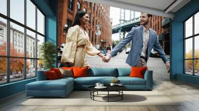 Love story in New York. Indian woman in bright yellow clothes and handsome American man hold each other hands walking around the New York Wall mural