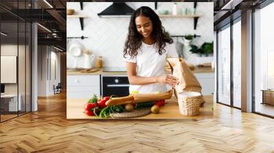 Smiled beautiful girl is putting packages with  food on the table on the modern kitchen Wall mural