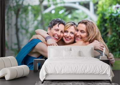 Three happy mature female friends hugging together and looking to camera Wall mural