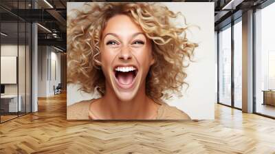 A joyful woman with curly hair laughing heartily against a light background in a cheerful indoor setting Wall mural