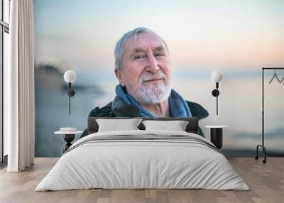 Gray-haired bearded man with blue eyes in green coat on in the beach at sunrise Wall mural