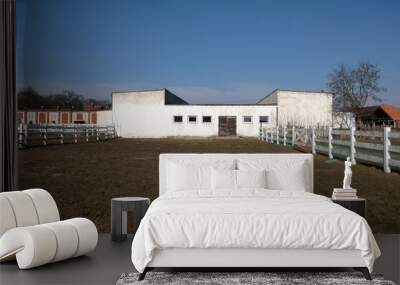 Brick stable building and paddock for horses fenced with a white wooden fence Wall mural