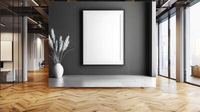 A large empty picture frame hangs on a dark grey wall in a modern interior. A vase of dried grass adds a touch of natural texture to the minimalist design. Wall mural