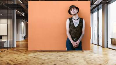 Tattooed person from the lgbt community in casual attire posing on an orange wall. Wall mural