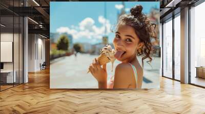 Funny teenage girl or young woman looking over her shoulder while licking melting ice cream on hot summer street, tongue visible, copy space on blurred city background Wall mural