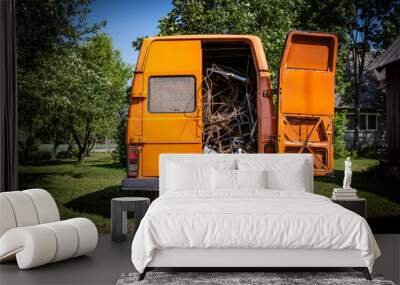 Rear view of an old orange vintage van with the right back door opened filled with scrape metal, waiting to be recycled in a natural green yard with trees and lawn under the summer sun Wall mural