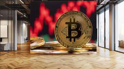 Gold Bitcoin coin stands sharply in front of a blurred red stock market chart, symbolizing financial risk Wall mural