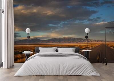 long straight desert road during sunset, Image shows the road in the Nevada desert during the golden hour giving off a beautiful scenic view of the desert and the mountains Wall mural