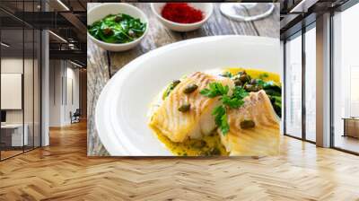 Fish dish - fried cod with spinach and capers in saffron sauce on wooden table
 Wall mural