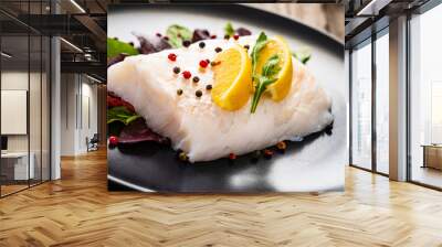 Fresh raw cod with vegetable leaves and lemon  on black plateon on wooden table Wall mural