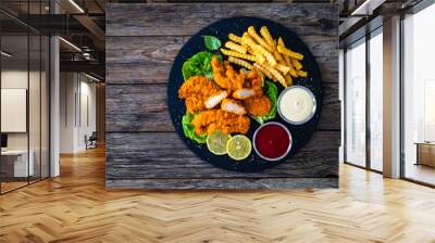 Fried breaded chicken nuggets served with French fries and vegetables on wooden table
 Wall mural