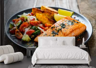 Fried salmon fillet with fried potatoes, lime and vegetable salad served on black plate on wooden table Wall mural