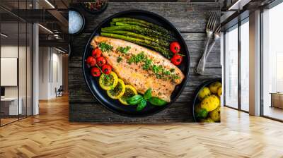 Roasted trout fillet with asparagus and vegetables served on black plate on wooden table
 Wall mural