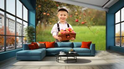 Smiling little boy with apples in an autumn orchard. Wall mural