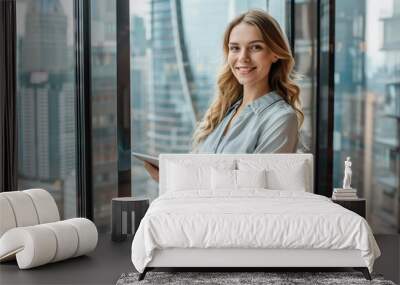 Young business woman standing in modern office, holding tablet and smiling at camera. Wall mural