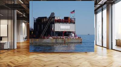 A big barge with work equipment anchored close to an ocean beach to perform oil well work Wall mural