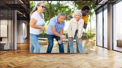 A group of multiracial middle aged mixed-sex adult people playing petanque game outdoors in public park on a sunny day Wall mural