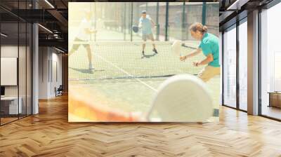 Adult and elderly men paddle tennis doubles players play against two men on tennis court Wall mural