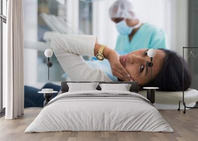 Adult Latina suffering from toothache lying on dental chair waiting for qualified medical aids from professional dentist Wall mural