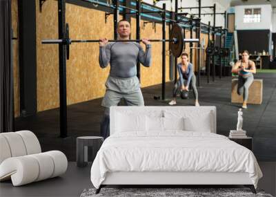 Adult male bodybuilder performing strength and endurance exercises during group barbell lifting in modern CrossFit class Wall mural