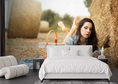 Adult topless woman lying with wine and phone during picnic in hay field Wall mural