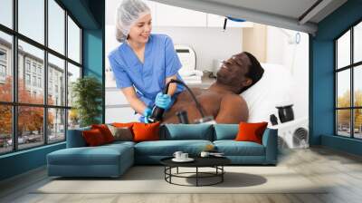 African male patient getting fat reduction skin lifting body treatment by female cosmetologist in modern clinic Wall mural