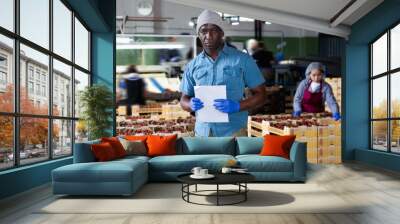 Afro american man supervisor controlling quality of cherry sorting at fruit warehouse Wall mural