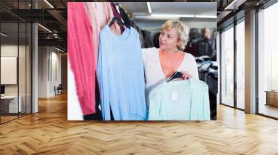 blonde woman buyer choosing color cardigan in the dress shop indoors Wall mural